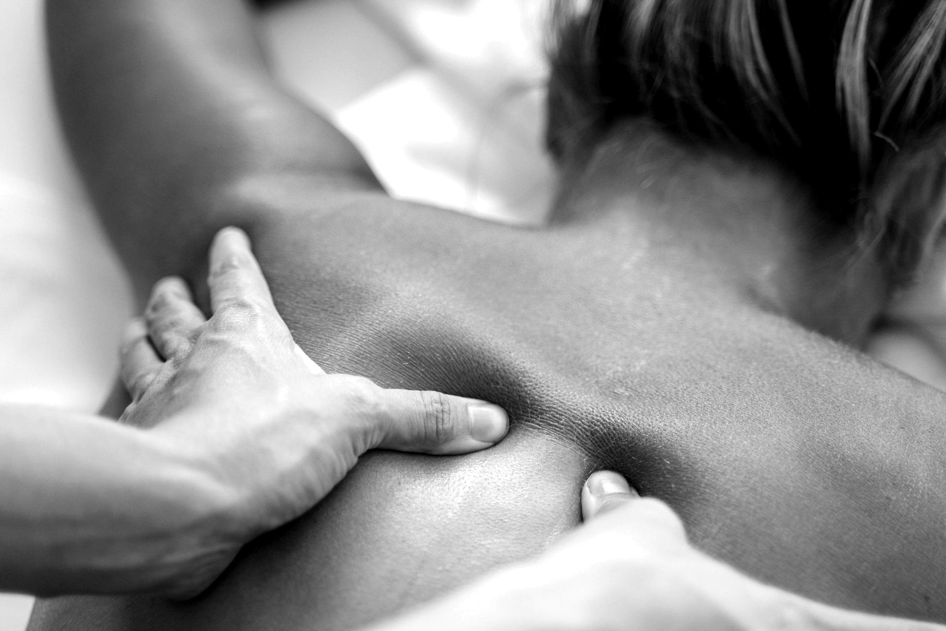 Black-and-white detail of hands applying targeted pressure during massage.